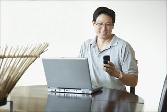 Japanese man using laptop and checking cell phone at table