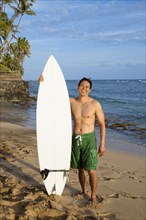 Japanese man holding surfboard on beach
