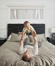 Father lifting son on bed in bedroom