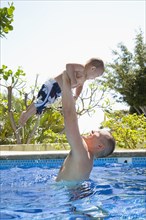 Father lifting son in swimming pool
