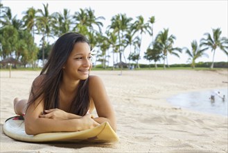 Mixed race girl on beach with surfboard