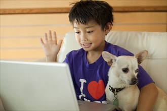 Mixed race boy using laptop and hugging dog