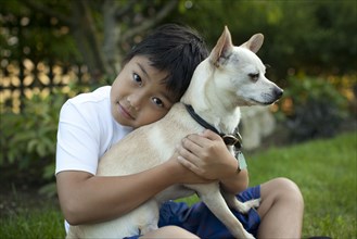 Mixed race boy hugging dog outdoors