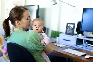 Caucasian mother working in home office and holding baby