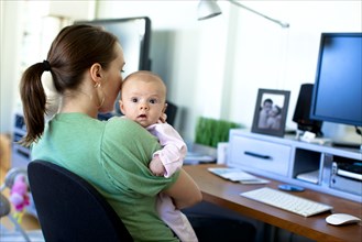 Caucasian mother working in home office and holding baby