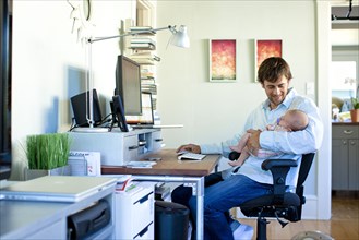 Caucasian father working in home office and holding baby