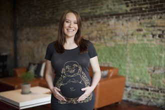 Smiling pregnant Caucasian woman holding stomach