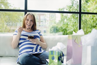 Pregnant Caucasian woman eating on sofa at baby shower