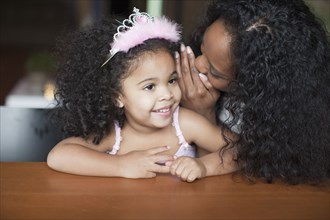 Mixed race mother whispering to daughter