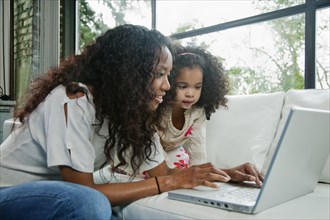 Mixed race mother and daughter using laptop together