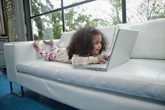 Mixed race girl using laptop on sofa