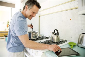Man cooking in kitchen and looking at digital tablet