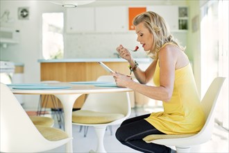 Caucasian woman eating and using digital tablet in dining room