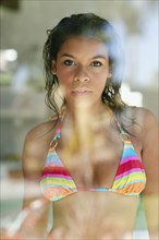 Serious mixed race woman in bikini behind window