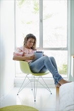 Mixed race woman sitting in chair using digital tablet