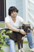 Mixed race man sitting on front stoop with dog