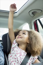 Mixed race girl sitting in car seat with arm out window