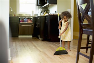 Mixed race girl sweeping kitchen floor