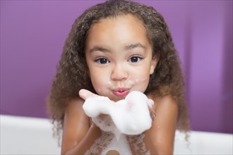 Mixed race girl playing with bubbles in bathtub