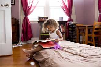 Mixed race girl reading in bedroom