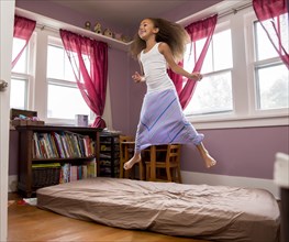 Mixed race girl jumping on bed