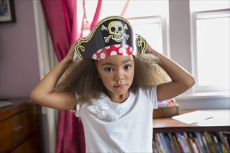 Mixed race girl wearing pirate hat in bedroom