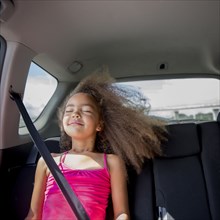 Mixed race girl enjoying wind in hair in back seat of car