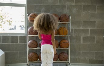 Mixed race girl picking basketball from rack