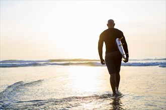 Mixed race man walking with surfboard on beach