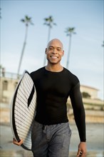 Mixed race man carrying surfboard on beach