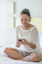 Mixed race woman using cell phone on bed