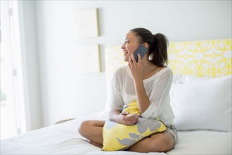 Mixed race woman talking on cell phone on bed