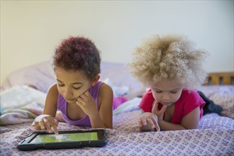 Mixed race sisters using digital tablets in bed