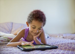 Mixed race girl using digital tablet in bed
