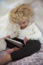 Mixed race girl using digital tablet under covers