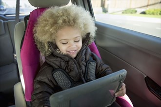 Mixed race girl using digital tablet in back seat of car