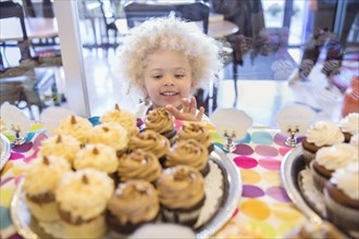 Mixed race girl picking cupcakes in bakery