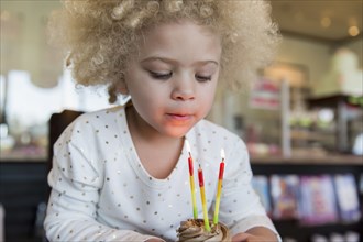 Mixed race girl blowing candles on cupcake