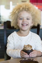 Mixed race girl having cupcake in bakery