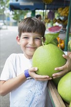 Caucasian boy holding large fruit at market
