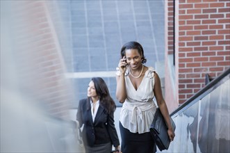 Black businesswoman talking on cell phone on escalator