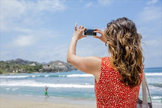 Mixed race woman taking pictures of tropical beach