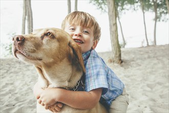 Boy hugging dog on wooded beach