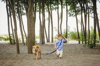 Boy walking dog on wooded beach
