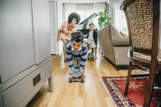 Mixed race family watching boy ride skateboard in living room