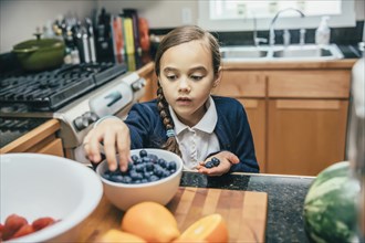 Mixed race girl picking blueberries from bowl in kitchen