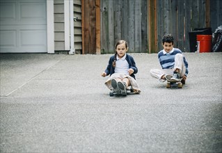 Mixed race brother and sister riding skateboards in driveway
