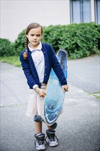Mixed race girl holding skateboard on sidewalk