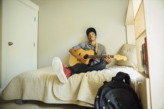 Mixed race boy playing guitar in bedroom