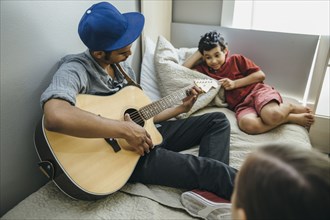 Mixed race boy watching brother playing guitar in bedroom